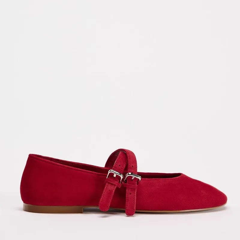 Red suede Mary Jane flat with a double buckle strap and brown sole, against a plain white background.