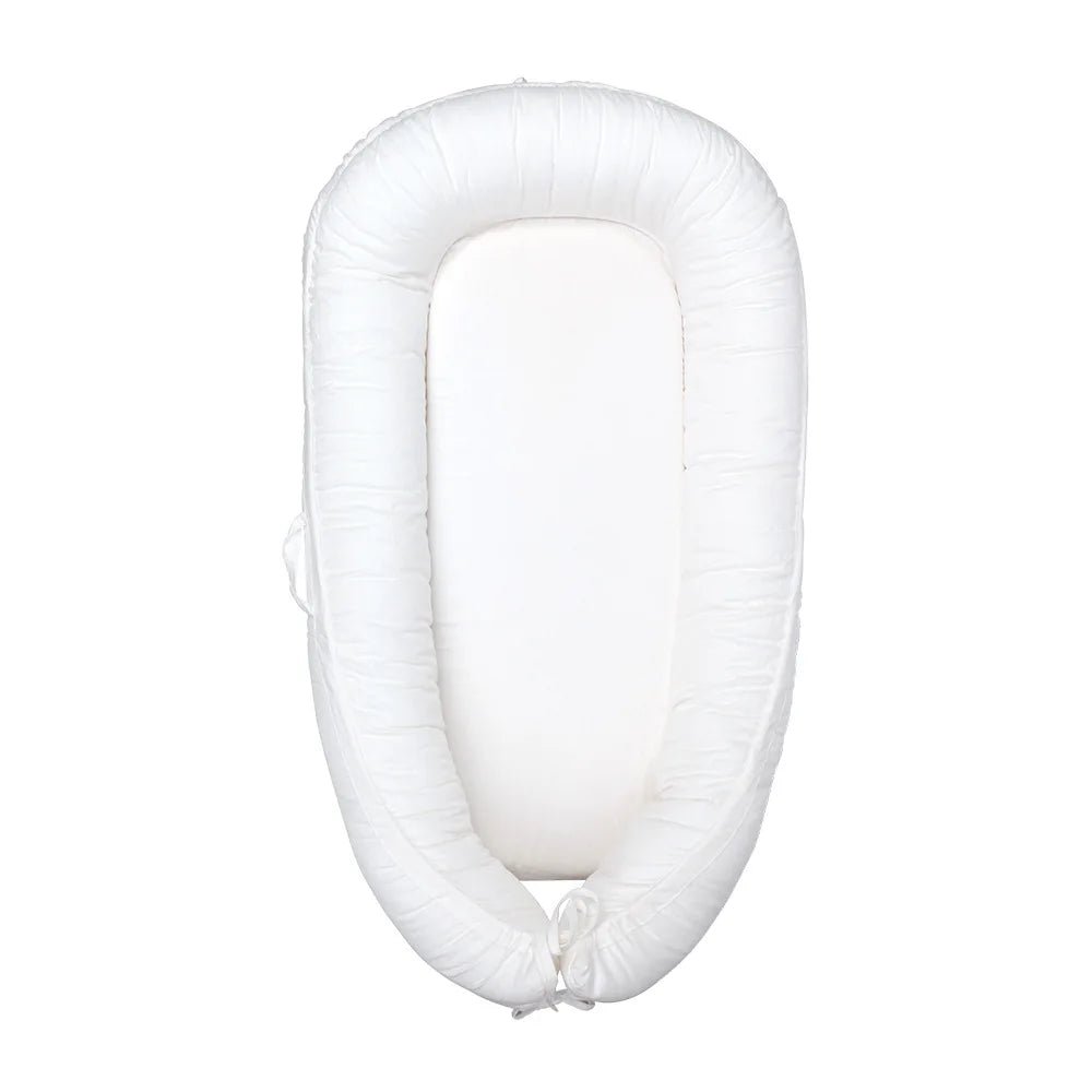 White cotton baby lounger with adjustable drawstring, featuring a soft, oval bumper design and a smooth interior surface, providing a cozy, secure environment for infants.