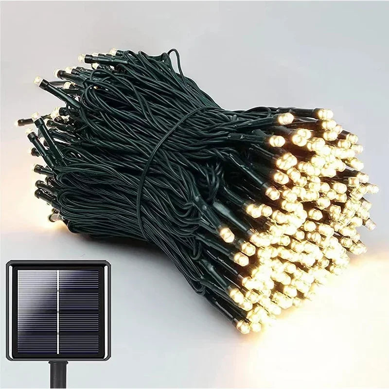 A bundle of warm white LED string lights with green wiring is shown, accompanied by a small solar panel in the bottom left corner for solar-powered use.