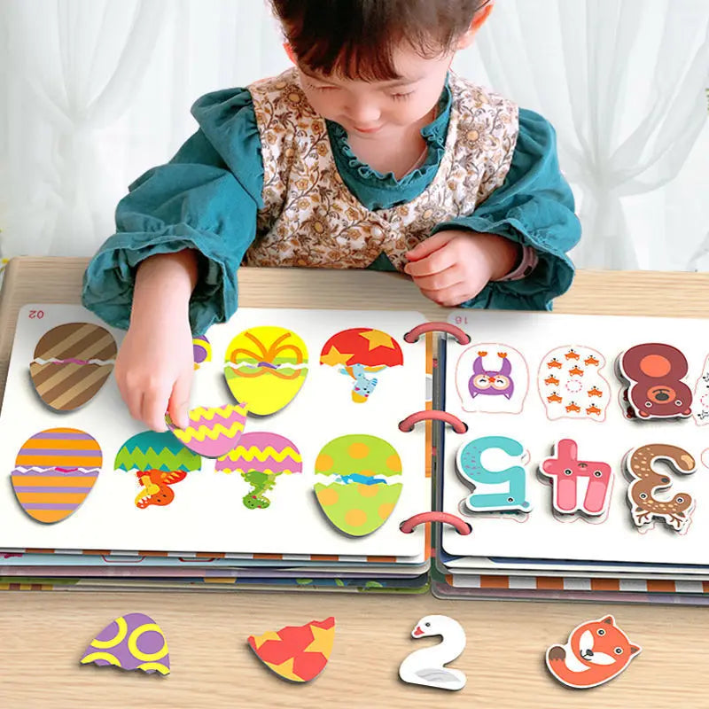 A child in a teal blouse plays with colorful, egg-shaped puzzle pieces on an open book, featuring various vibrant patterns and animal designs on a wooden table.