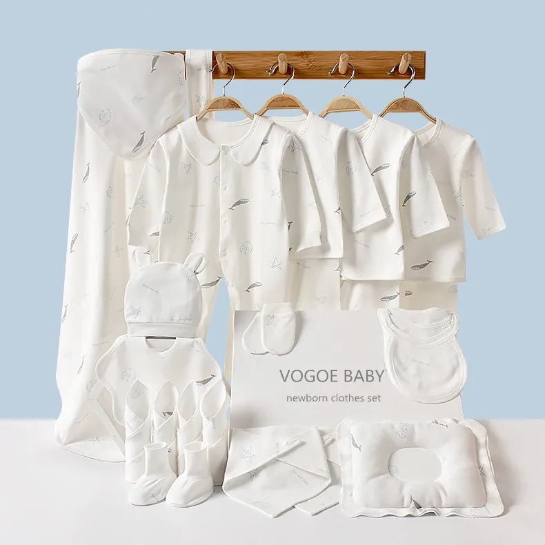A white newborn clothes set includes onesies, mittens, socks, bibs, a cap, a pillow, and a blanket with simple patterns, all arranged neatly against a light blue background.