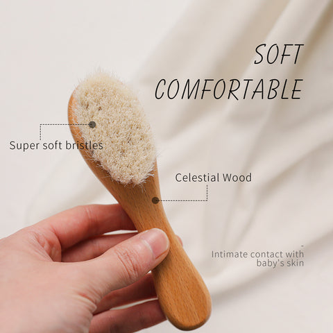 Hand holding a baby brush with super soft bristles and a wooden handle. Text overlays read "Soft Comfortable," "Super soft bristles," and "Celestial Wood." Background is a soft fabric.