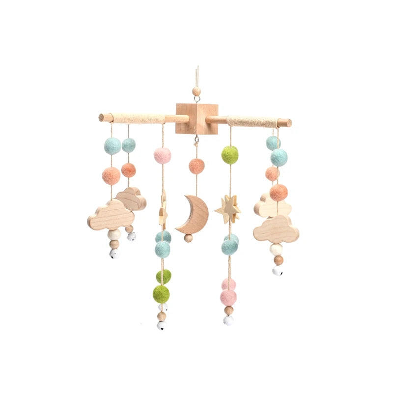 A wooden baby mobile with colorful felt balls and shapes, including clouds, a crescent moon, and stars, hanging from strings.
