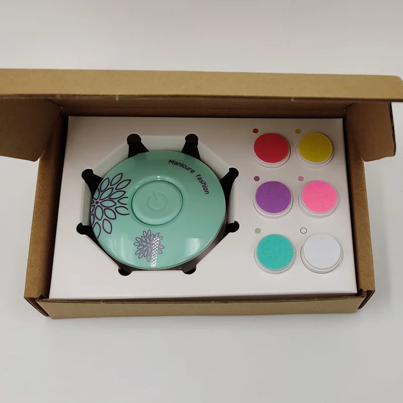 Open box containing a mint green manicure device with a floral pattern, labeled "Manicure Fashion," and six colored nail powders in red, yellow, pink, purple, teal, and white.