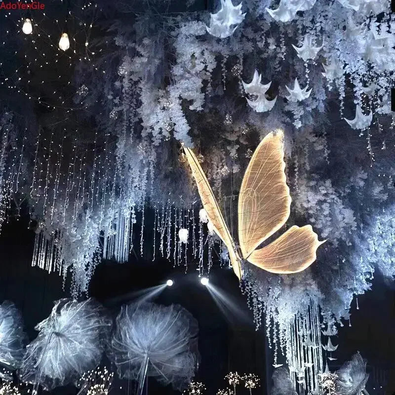 A glowing butterfly hangs amid ethereal decorations of cascading flowers and lights, creating a dreamy, celestial atmosphere with illuminated fabric-like structures below.