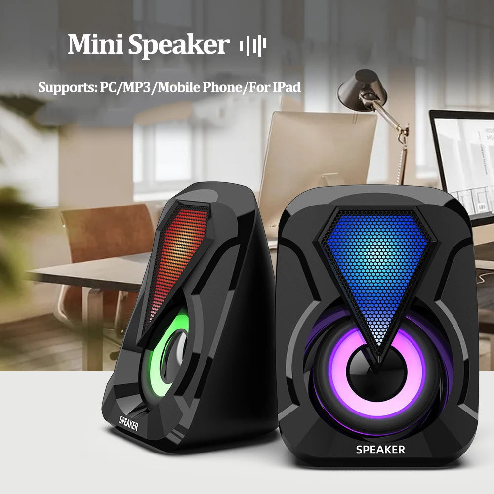 Mini speakers with colorful LED lights, one red and green, the other blue and purple, placed on a desk in an office setting. They support PC, MP3, mobile phones, and iPads.