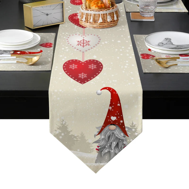 Festive table setting with a beige runner featuring red hearts and snowflakes, a gnome with a red hat, gold cutlery, white plates, and a basket of bread on a dark table.