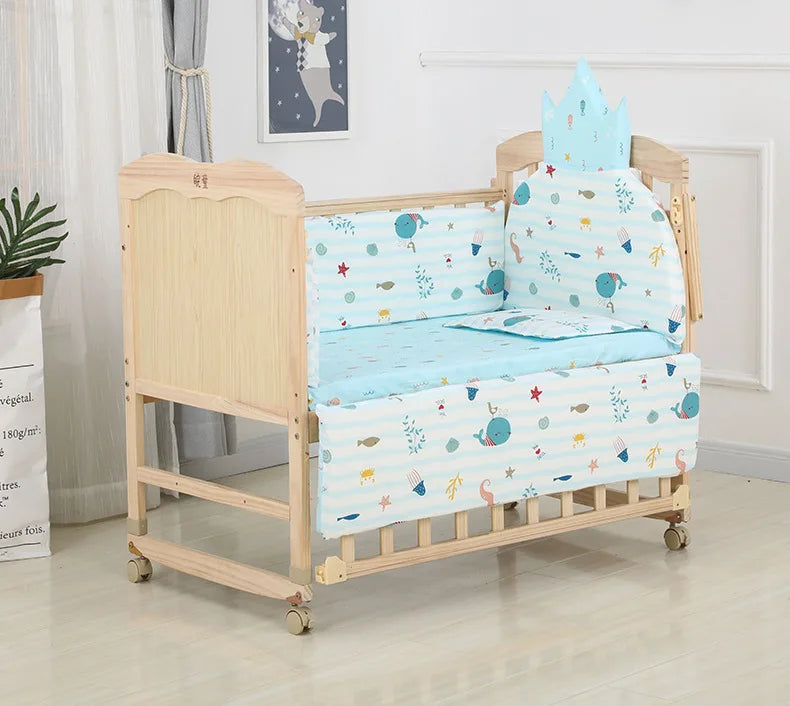 Wooden baby crib with blue ocean-themed bedding featuring whales and starfish. The crib has a cushioned crown-shaped headboard and is set in a bright room with decor.