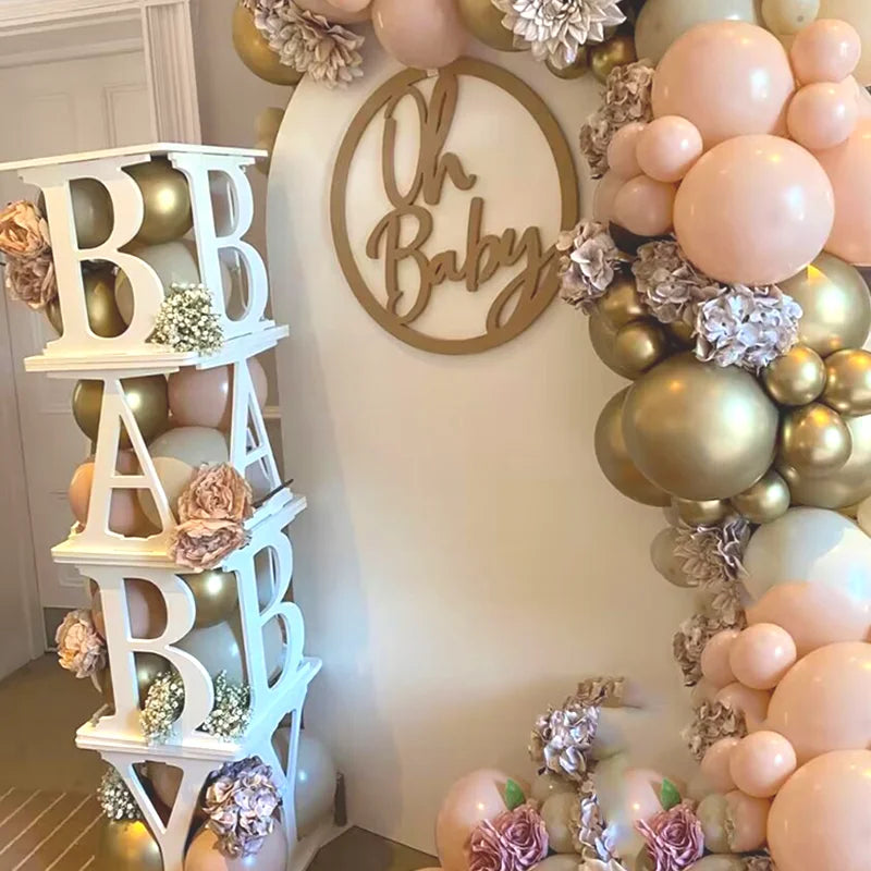 Baby shower decoration with pastel and gold balloons, floral accents, and a sign reading "Oh Baby." White blocks spell "BABY." Elegant and festive atmosphere.