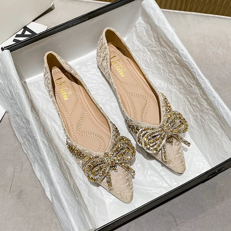 Elegant beige flats with intricate gold and silver embellishments and a sparkling bow detail on the toe, displayed in an open shoebox lined with white tissue paper.
