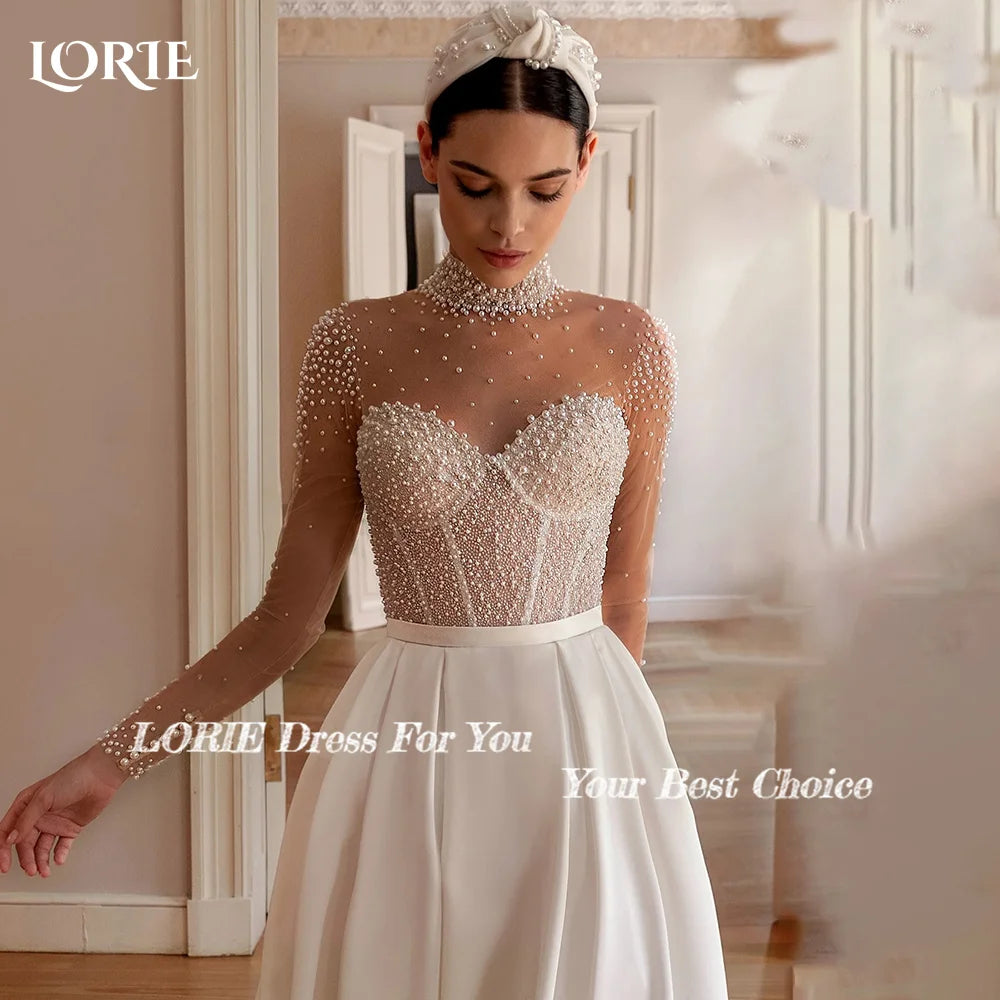A woman in a wedding dress with a pearl-embellished sheer top and a white satin skirt. She wears a pearl headband and is in a softly lit, elegant room.