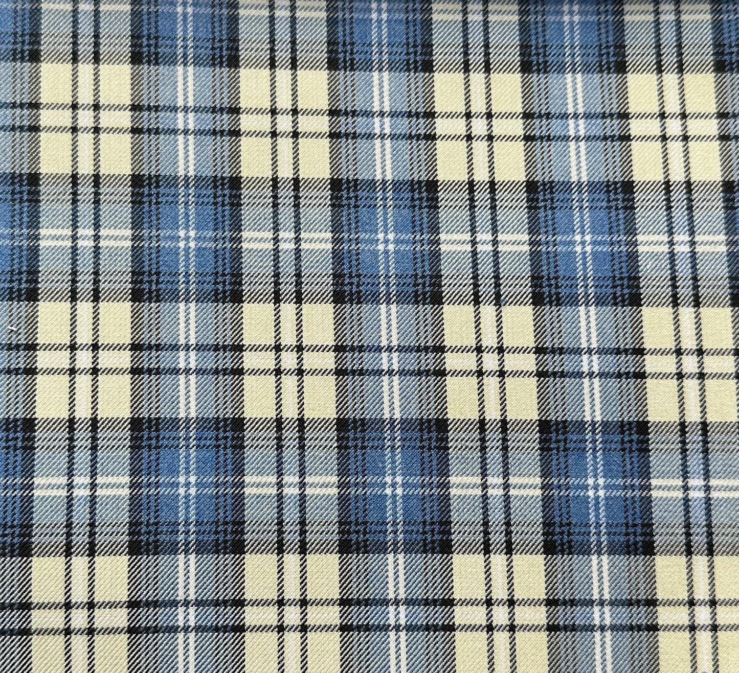 Close-up of a plaid fabric featuring a pattern of beige, blue, and black intersecting stripes forming squares. The design creates a classic, symmetrical tartan look.