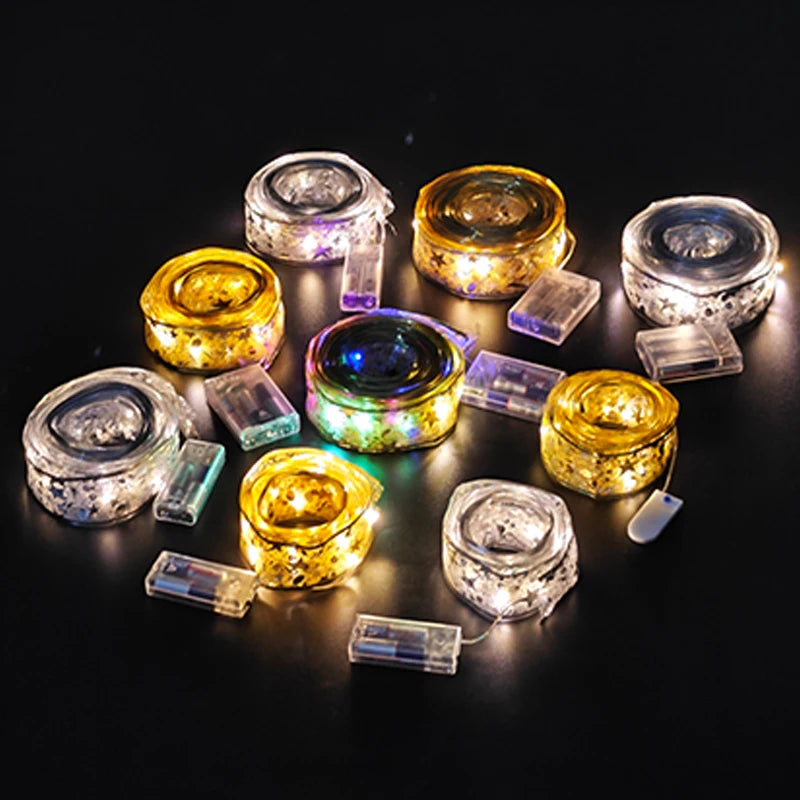 Coiled LED fairy lights in varying colors, including yellow, white, and multicolored, with attached battery packs, arranged in a circle on a dark background.