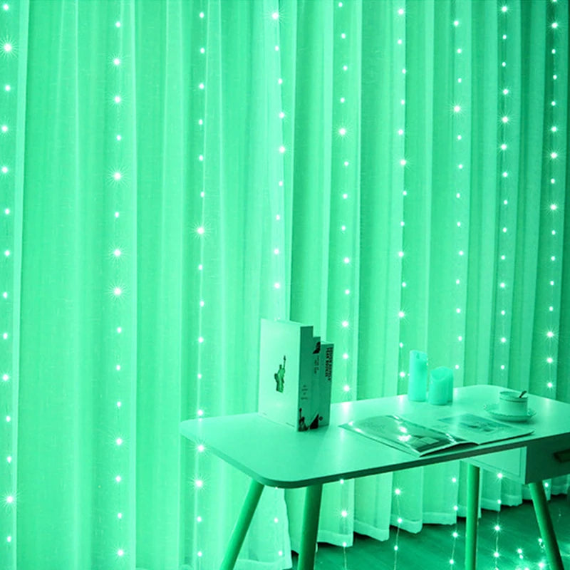 A room with green LED string lights hanging over sheer curtains. A white table holds an open book, magazines, candles, and a cup, creating a cozy ambiance.