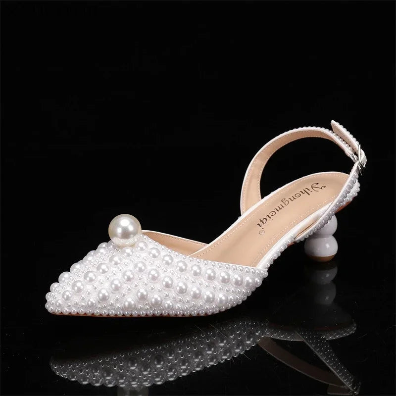 Elegant white sandal with pearl embellishments, featuring a large pearl on the toe and a unique spherical heel, displayed against a black background.