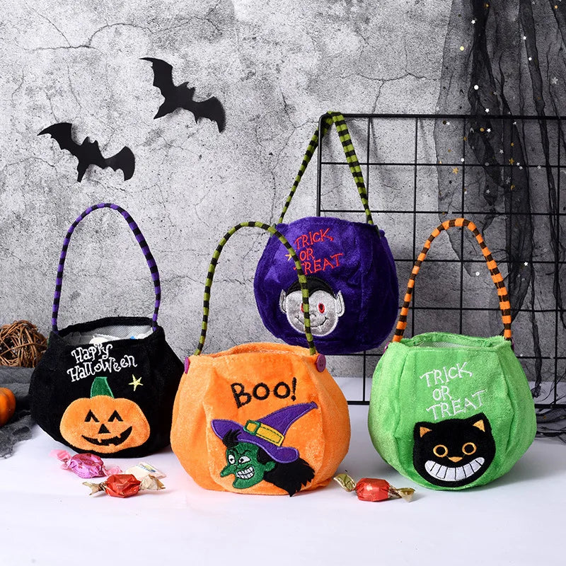 Four colorful Halloween-themed treat bags with handles, featuring designs like a pumpkin, witch, vampire, and cat, are displayed with candy on a white surface. Bats are on the wall behind.