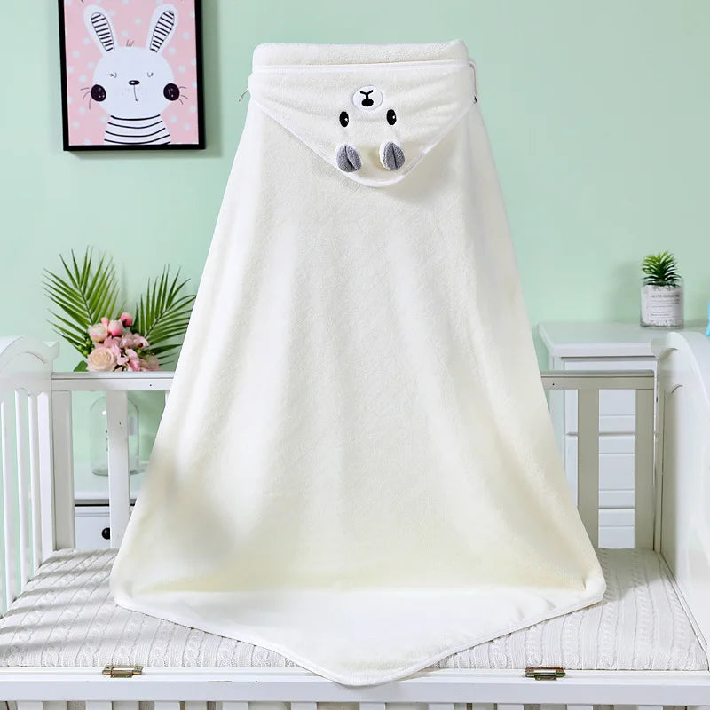 A soft, cream-colored baby towel with a bear face hood is draped on a crib. A bunny picture is framed on the pastel green wall, with pink flowers and greenery nearby.