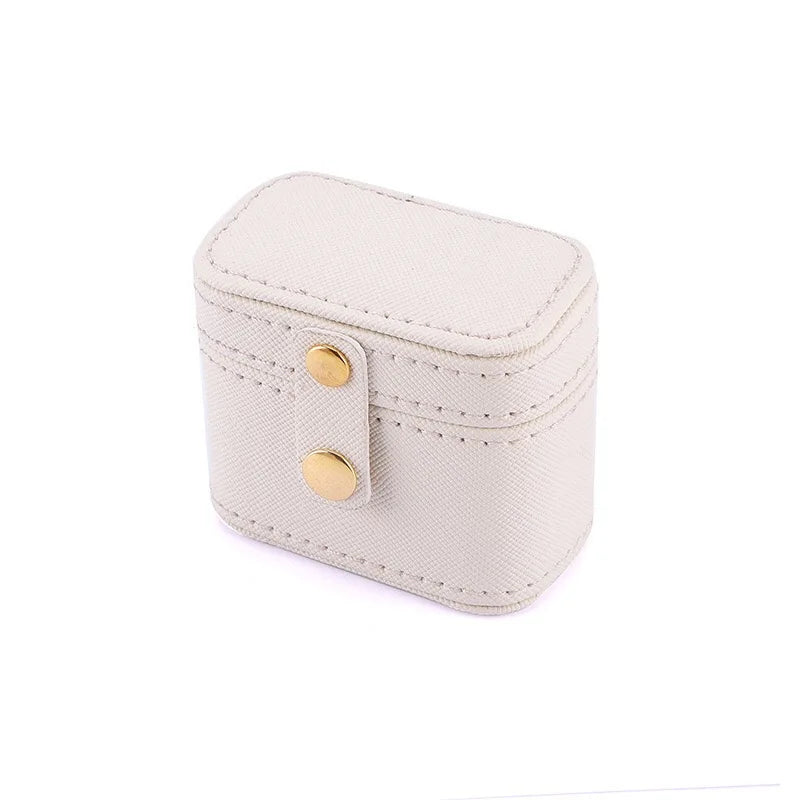 Small beige fabric jewelry box with a rectangular shape and rounded edges, featuring two gold snap buttons on the front. The box has decorative stitching along its edges.