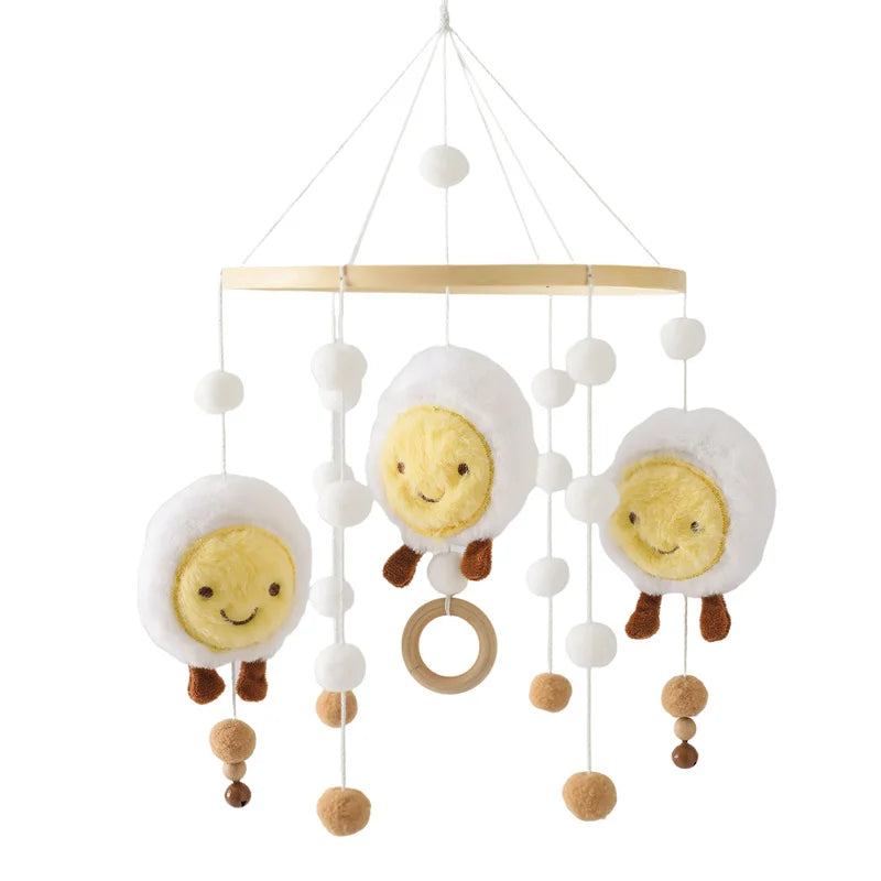 Hanging mobile with three plush sun figures in white clouds, surrounded by small white and brown pom-poms, featuring a wooden ring in the center.