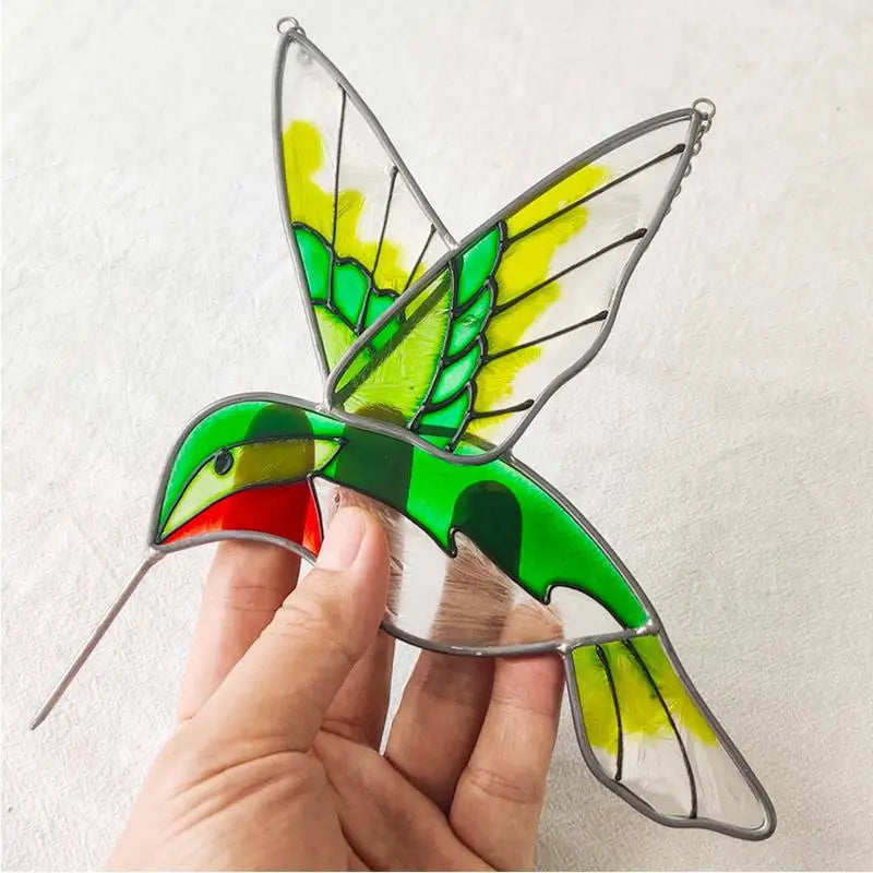 Stained glass hummingbird with vibrant green, yellow, and red colors, held in hand against a plain background. The intricate design captures light beautifully.