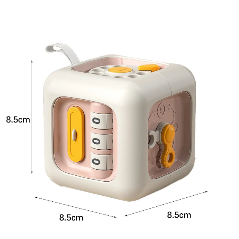 Interactive cube toy with various gadgets on each side, including dials, switches, and gears. Dimensions are 8.5cm by 8.5cm, with a soft pink and white color scheme.