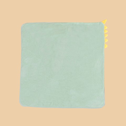 A square, light green blanket with rounded corners and small, yellow triangular spikes on the upper right edge, set against a beige background.