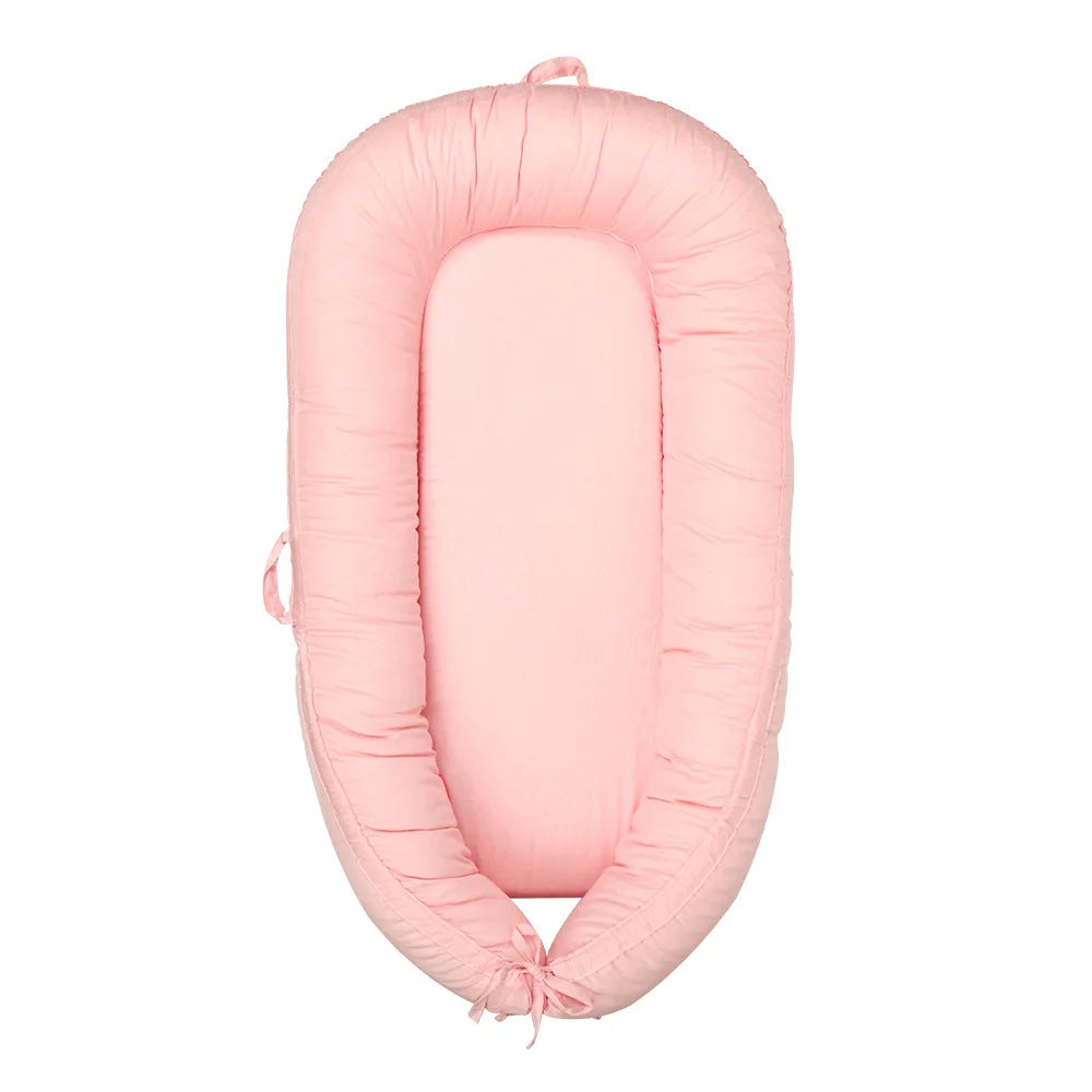 Pink baby nest with soft, padded sides and an oval shape. The mattress and sides are uniform in color, providing a cozy, secure sleeping environment for infants.