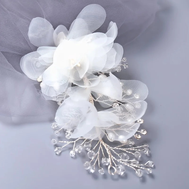 Elegant white chiffon flower accessory with delicate petals, pearl accents, and intricate crystal branches on a soft gray background. Perfect for bridal or formal occasions.