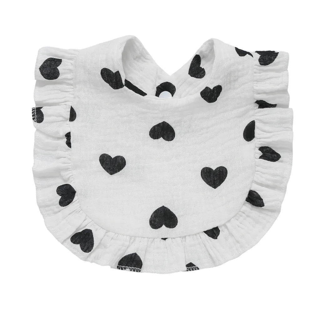 White baby bib with black heart patterns and a ruffled edge, designed for infants. The material appears soft, adding to the bib's functional and aesthetic appeal.