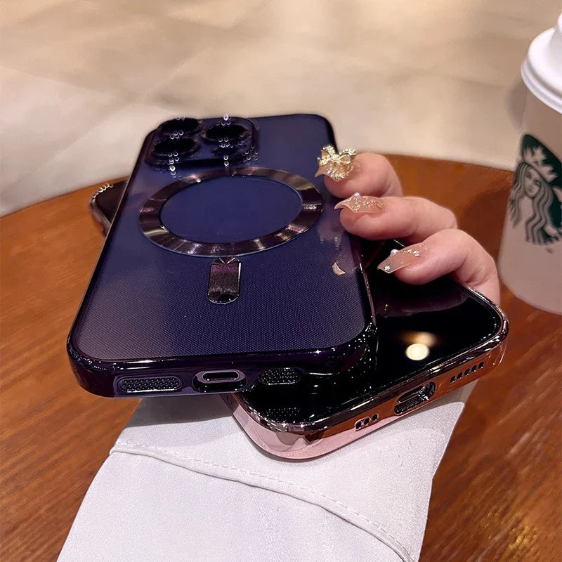 A hand with decorated nails holds two smartphones in shiny cases over a wooden table. A Starbucks cup is partially visible in the background.