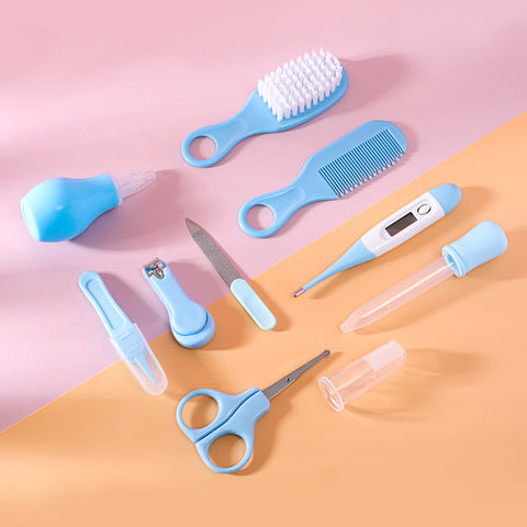 Baby grooming kit on pastel surface, featuring a soft-bristle brush, comb, nasal aspirator, nail clipper, scissors, file, thermometer, and dropper, all in blue and white.