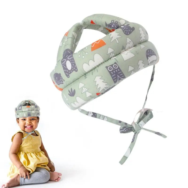 Cushioned baby safety helmet, green with animal patterns, shown alone and worn by a smiling baby in a yellow dress sitting on the floor.