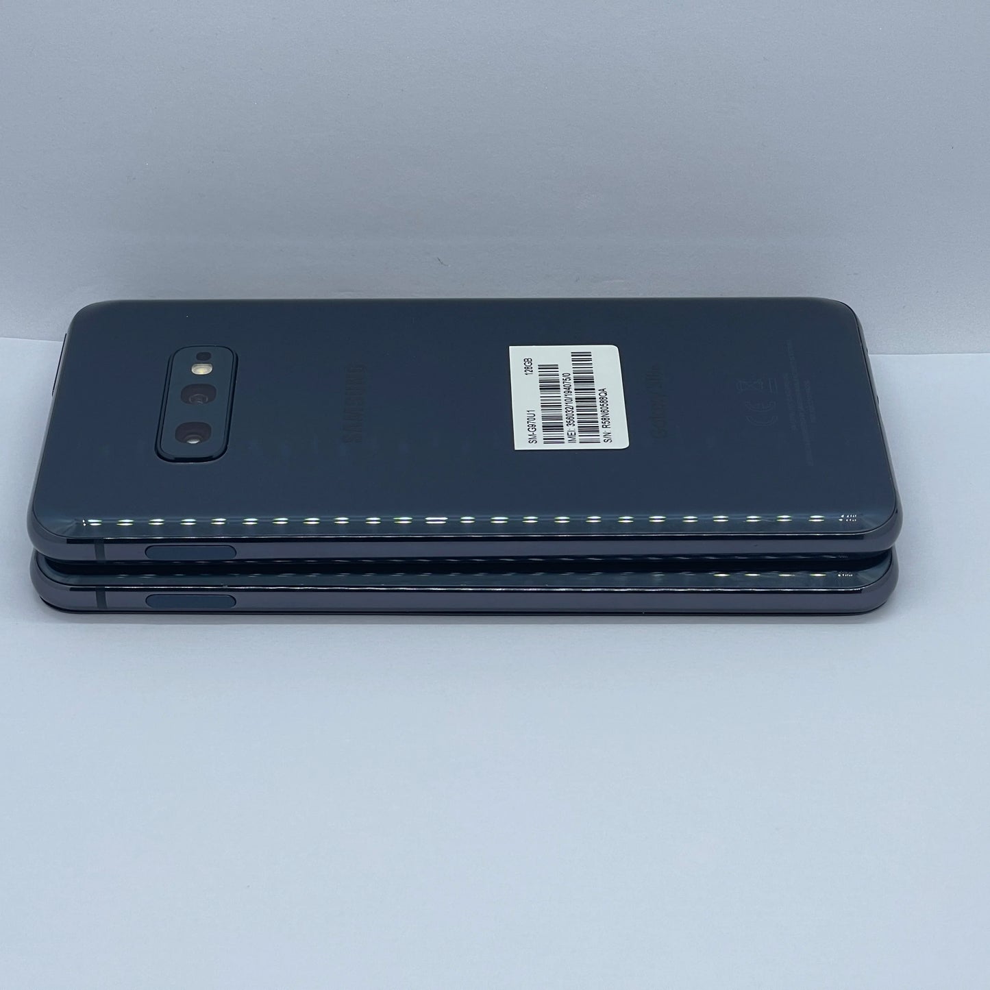 Two stacked smartphones with a dark gray back, featuring dual rear cameras and a barcode label on one device, placed on a white background.