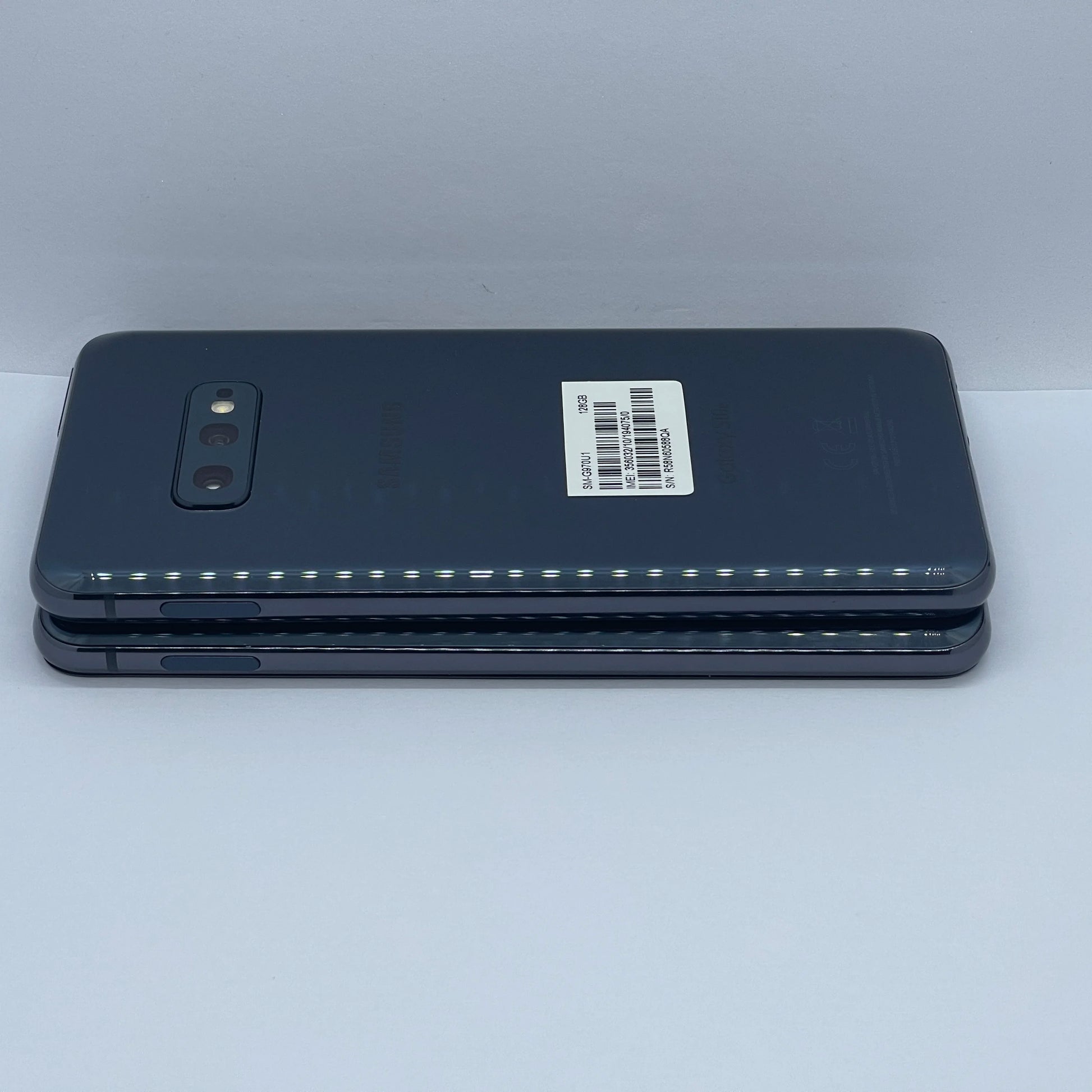 Two stacked smartphones with a dark gray back, featuring dual rear cameras and a barcode label on one device, placed on a white background.