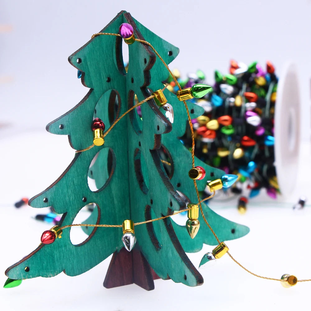Wooden green Christmas tree ornament with circular cutouts, decorated with a string of colorful bulb lights. A spool of multi-colored lights is visible in the background.