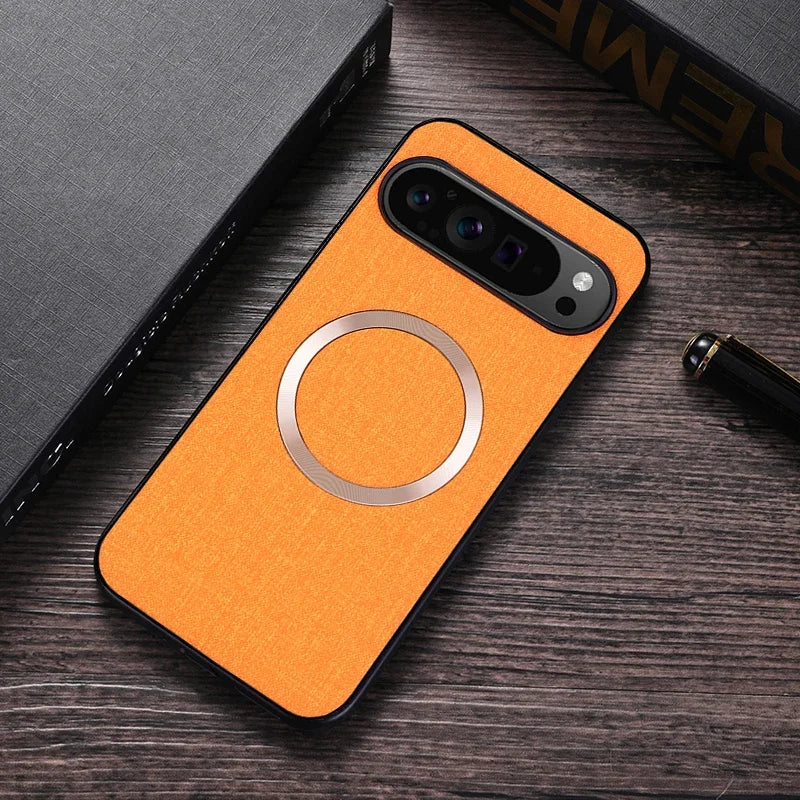 Orange smartphone case with a metallic ring design on a wooden table. Nearby, there is a black pen and a gray book with textured covers.