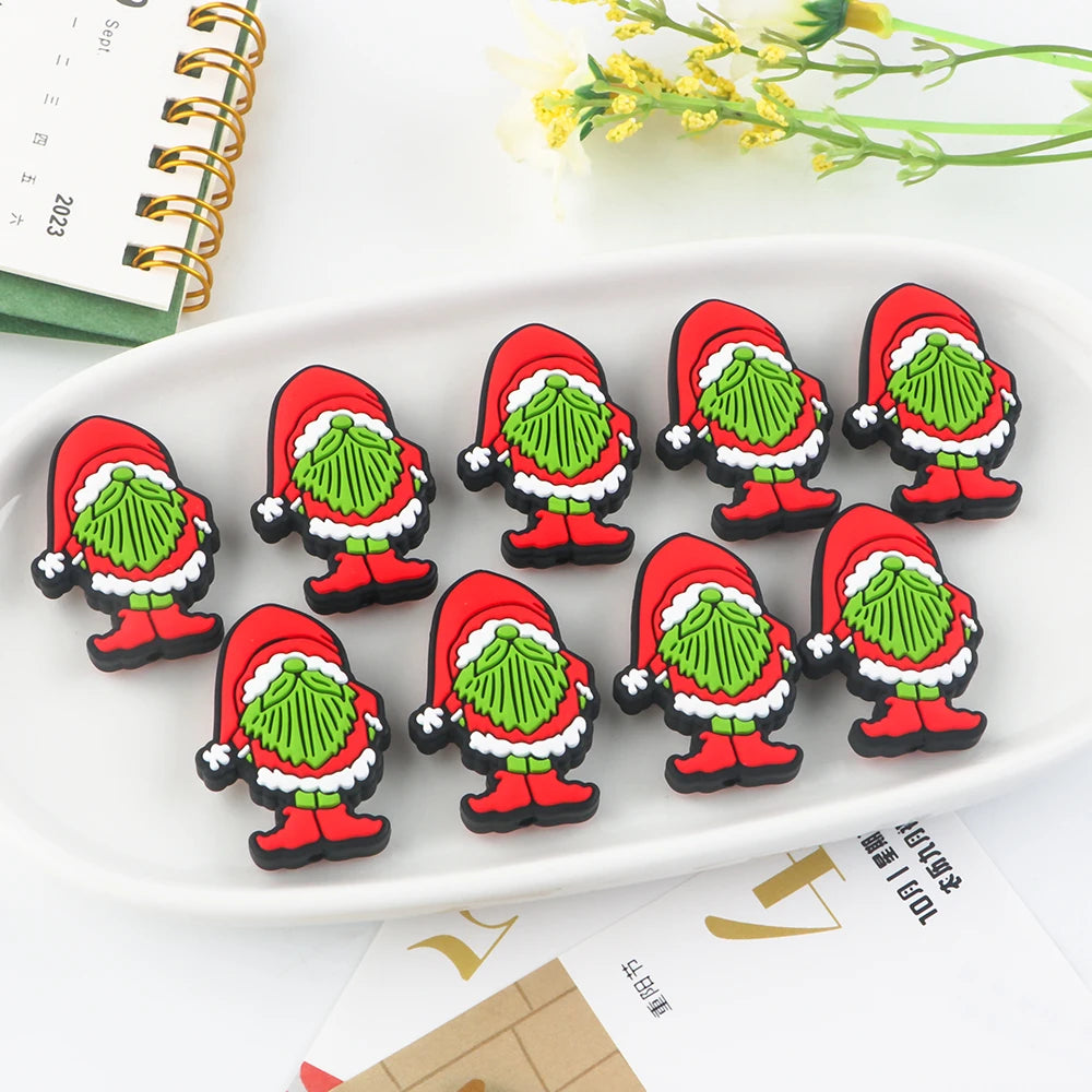 Ten cartoonish, green-faced figures dressed as Santa Claus are arranged on a white dish with a calendar and flowers nearby.