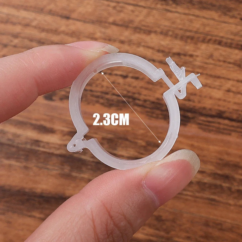 Close-up of fingers holding a clear, circular plastic item with a measurement of 2.3 cm across. The item appears small and lightweight, set against a wooden background.