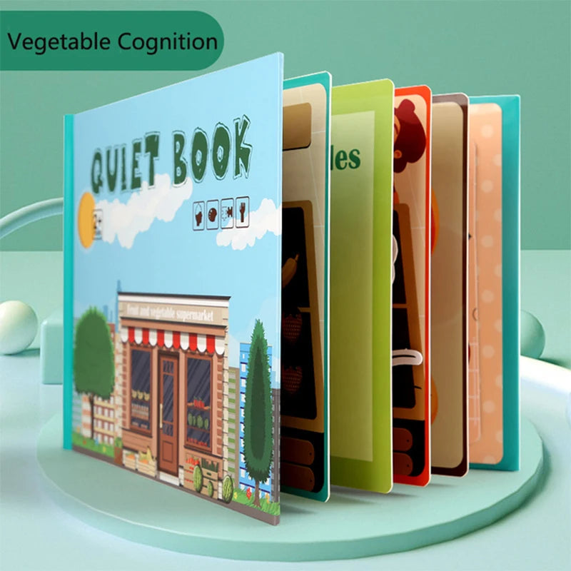 Children's quiet book with a vibrant cover depicting a store and trees, titled "Vegetable Cognition." Multiple colorful, partially open pages are visible, set against a green background.