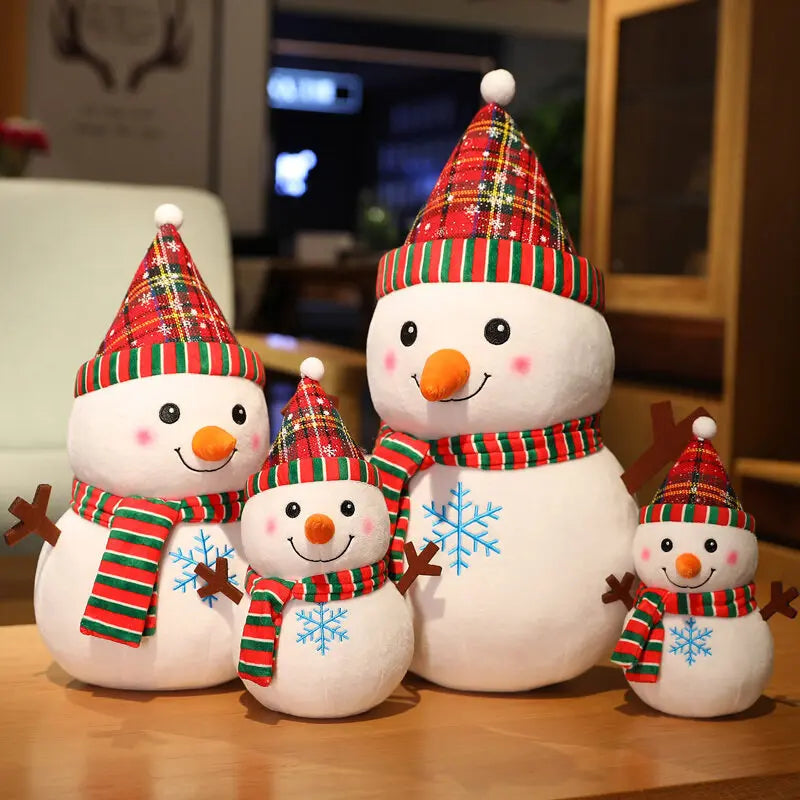 Four plush snowmen of varying sizes with red and green striped hats and scarves, orange noses, and blue snowflake designs, sit on a wooden table in a cozy room.