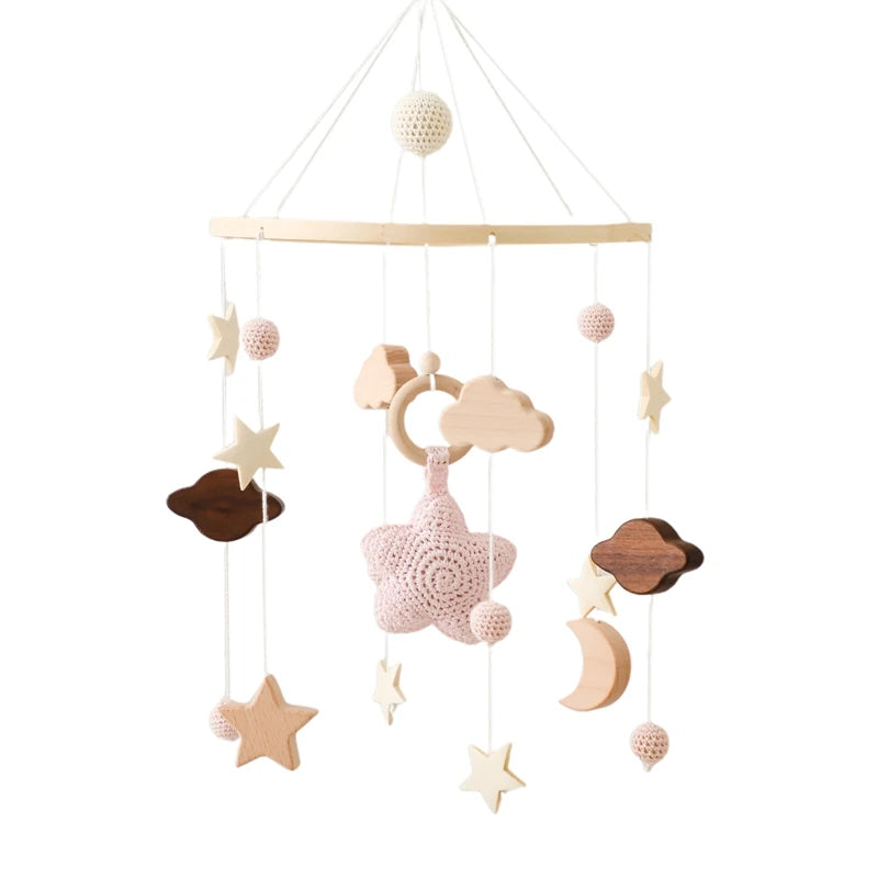 A delicate baby mobile with crochet and wooden elements, featuring stars, clouds, a moon, and a central pink crochet star, suspended on white strings from a wooden ring.