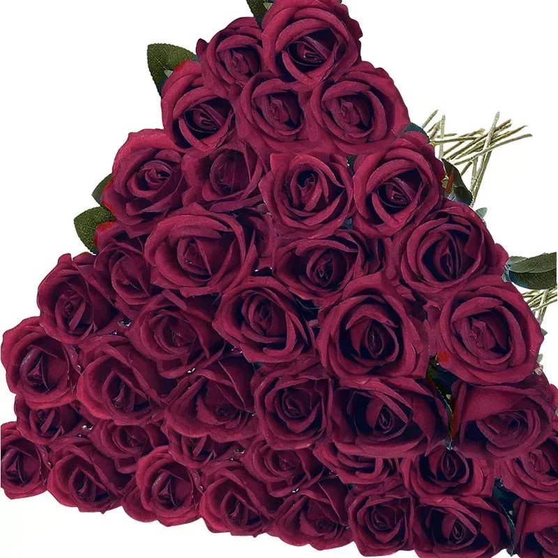 A bouquet of deep red roses, densely packed and arranged in a triangular shape, with hints of green leaves and visible stems, set against a white background.