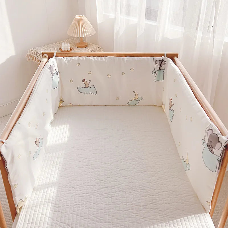 A cozy wooden crib with soft quilted bedding and cute animal-themed bumpers. A small table with a lamp and sheer curtains allow sunlight to softly illuminate the room.