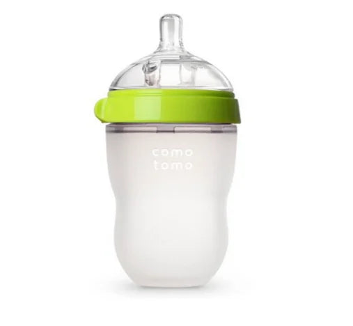 A silicone baby bottle with a green cap and clear nipple, featuring "comotomo" branding. The design is ergonomic and includes a wide neck for easy cleaning and filling.