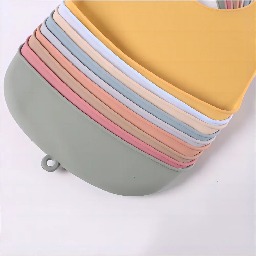 Stack of silicone bibs in pastel colors including green, pink, peach, blue, and yellow, displayed on a light background.