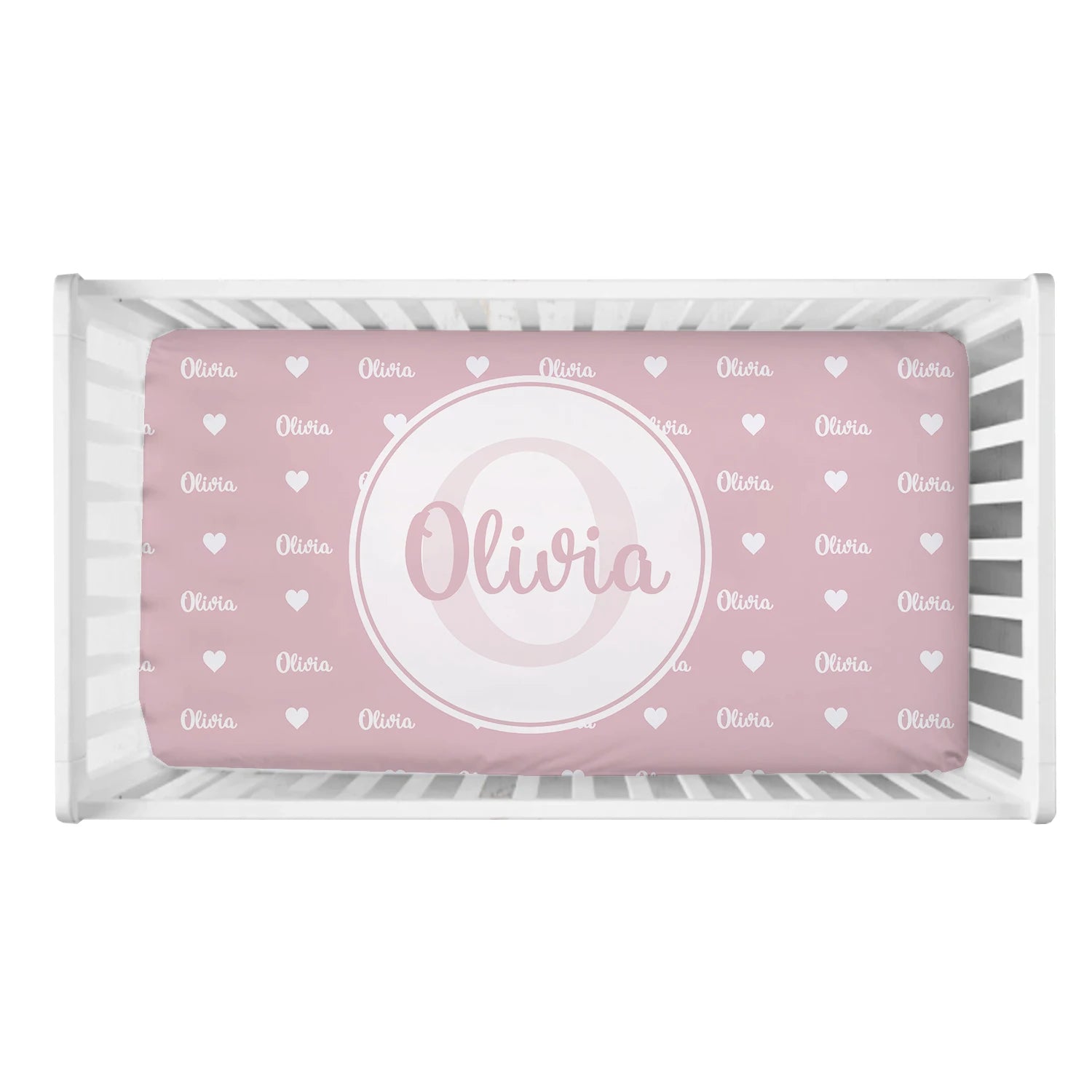 White crib with a pink mattress featuring "Olivia" in white, surrounded by small white hearts. A large circle in the center highlights the name in script font.