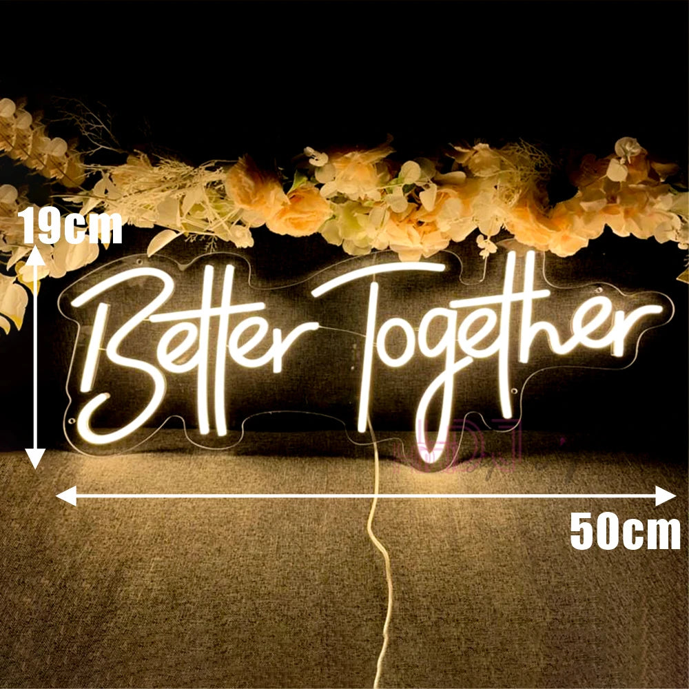 Neon sign reading "Better Together" measuring 19cm by 50cm. It is illuminated in warm light with decorative flowers above and a visible power cord below.