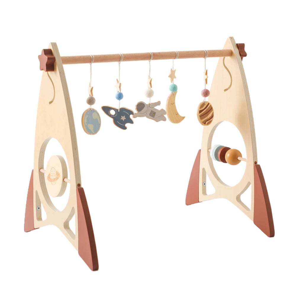 Wooden baby play gym with space-themed hanging toys, including planets, a rocket, and an astronaut. Features side circles with beads, all in natural and pastel colors.