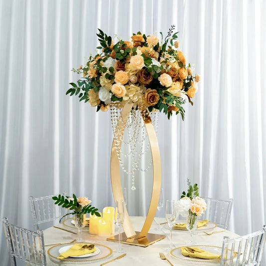 Elegant table setting with a tall floral centerpiece of peach and white roses, greenery, and hanging crystals. Surrounded by glassware, candles, and gold-accented dinnerware on a round table.