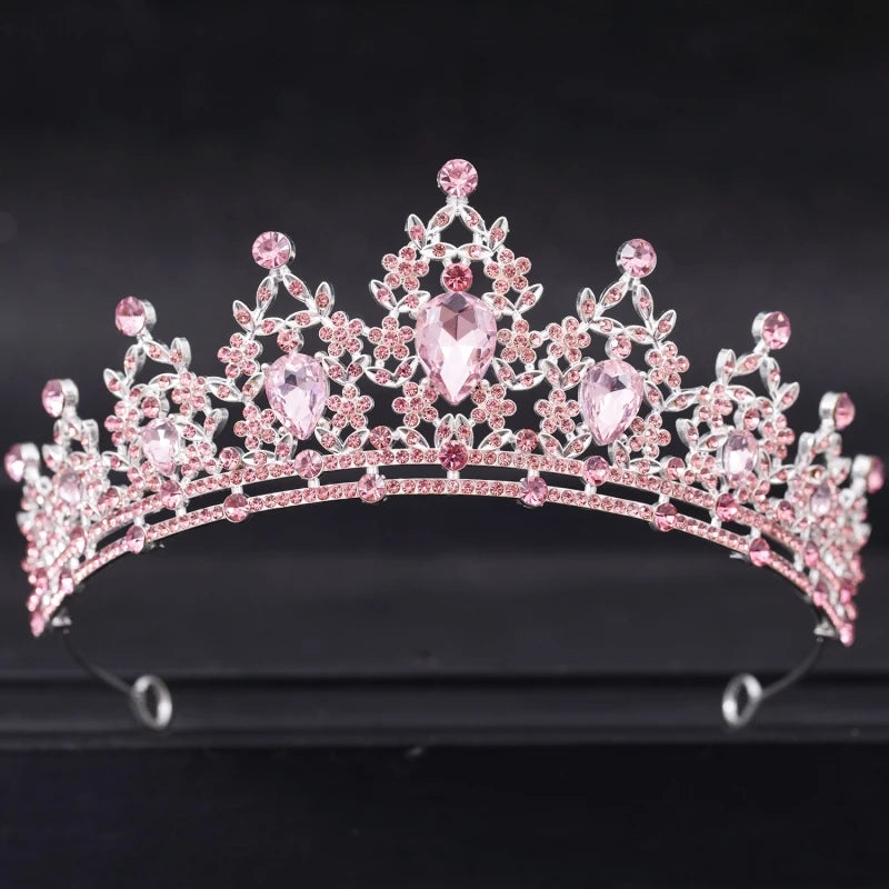 A sparkling tiara adorned with intricate pink gemstones and floral designs, set against a black background. The crown features several teardrop-shaped stones for emphasis.